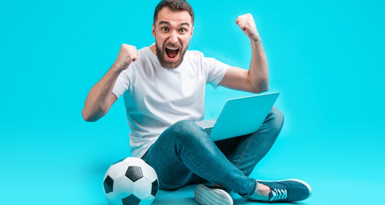 Apostador celebra un acierto junto a un balón de fútbol. Guía apuestas más/menos 2.5 goles.