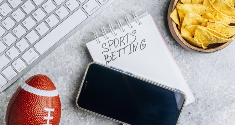 Imagen de un móvil, un balón de fútbol americano y una libreta. Glosario de apuestas deportivas.